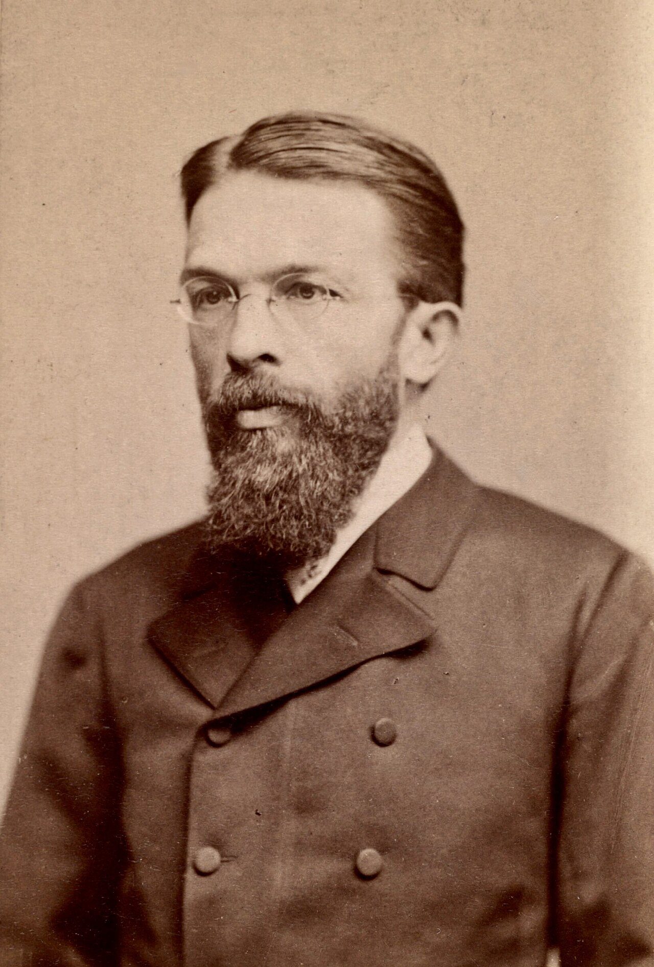 Carl Menger in late middle age, bearded and in a dark jacket and high collar, photographed in three-quarter profile against a plain studio background