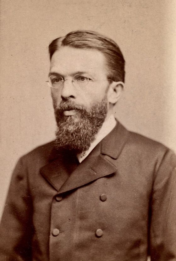 Carl Menger in late middle age, bearded and in a dark jacket and high collar, photographed in three-quarter profile against a plain studio background