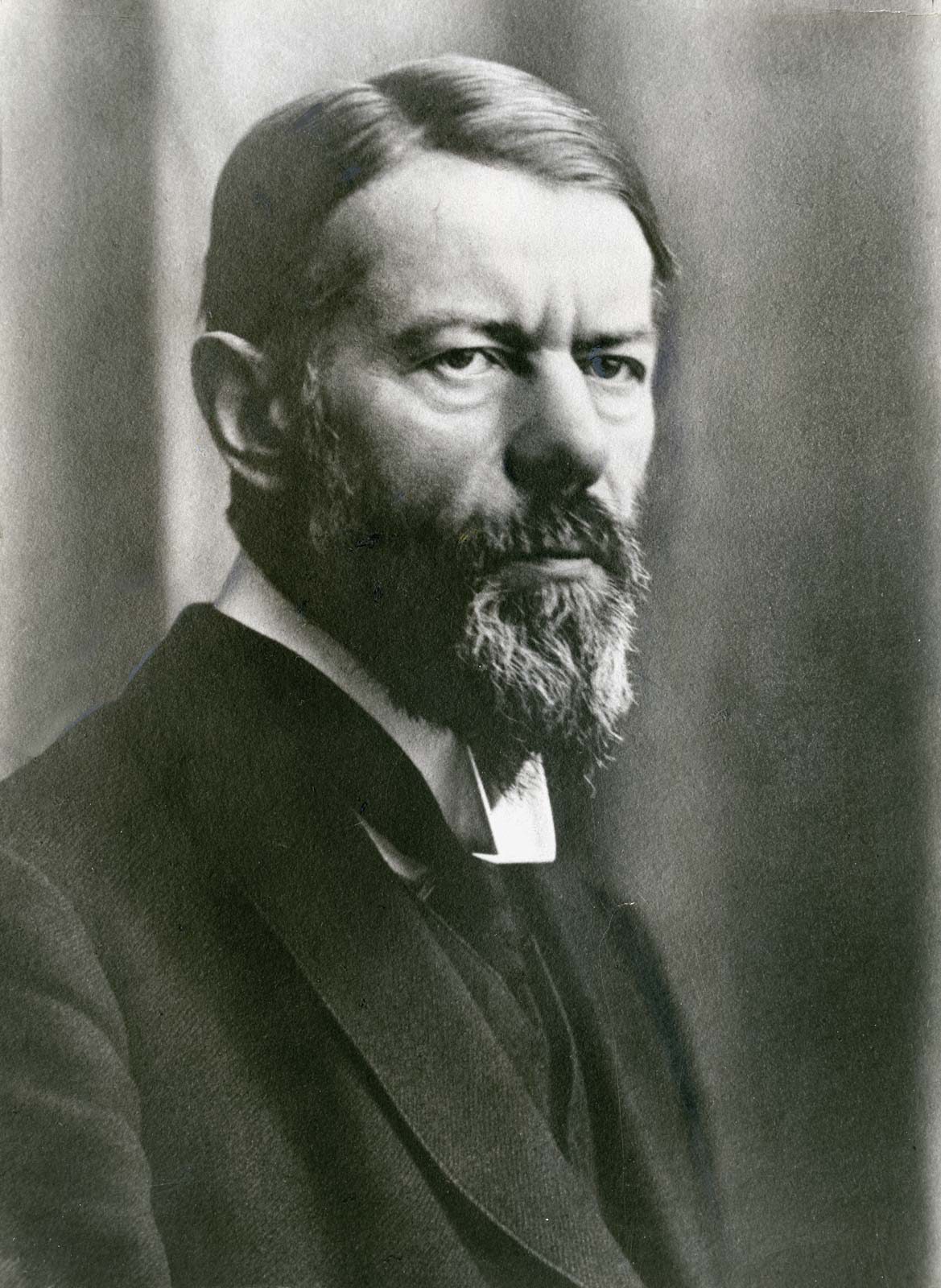 Max Weber in his fifties, with swept-back hair, a full greying beard and a hard frown, in a dark suit and a high white collar, photographed in three-quarter view