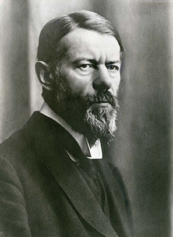 Max Weber in his fifties, with swept-back hair, a full greying beard and a hard frown, in a dark suit and a high white collar, photographed in three-quarter view