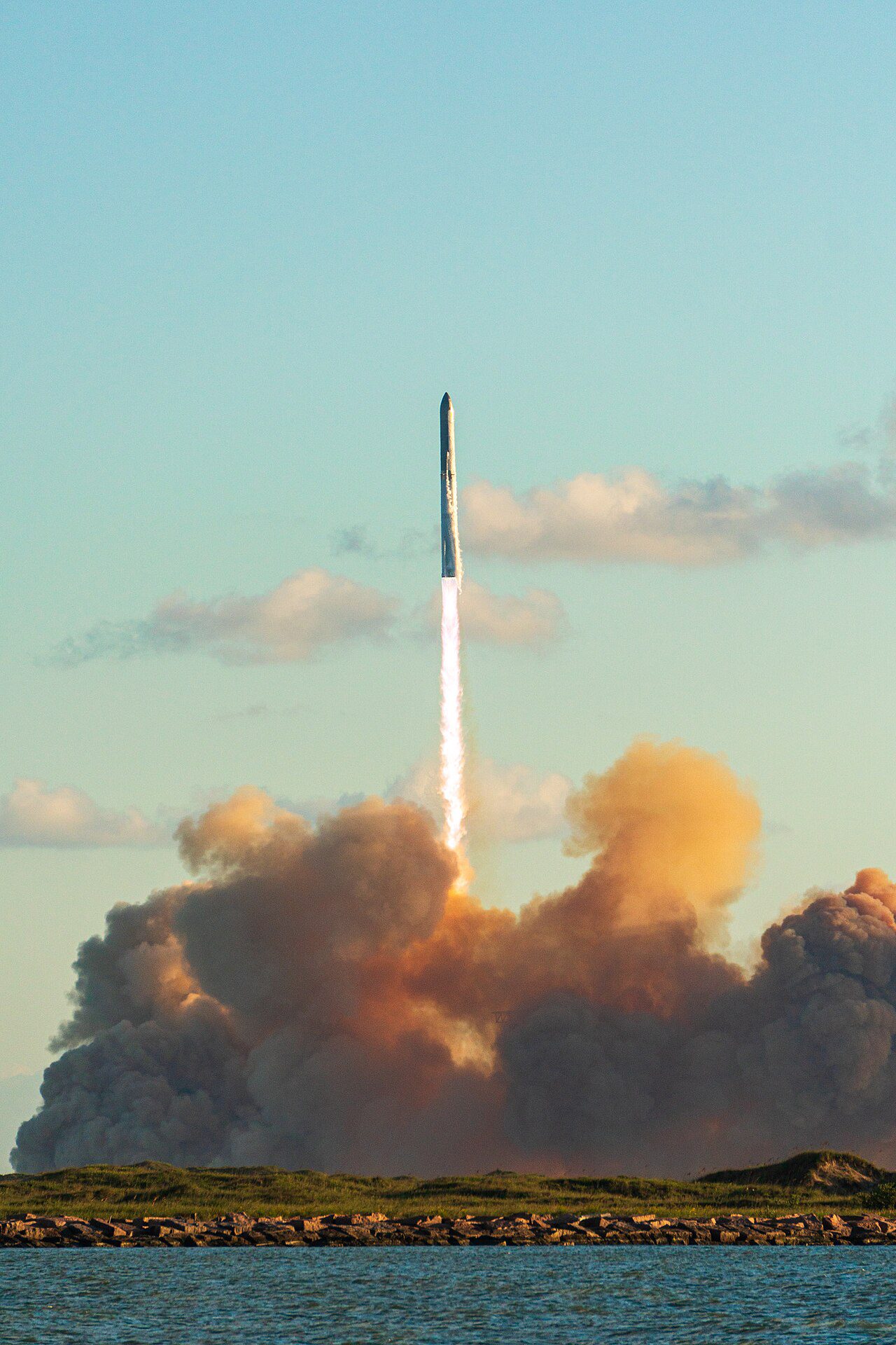 A Starship stack climbing away from its launch tower on a column of exhaust, seen against a pale sky